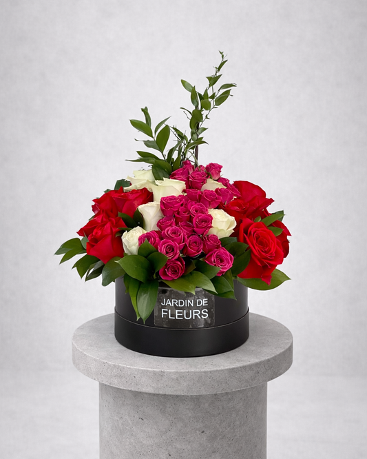 Bouquet of red, pink, and white roses in a black box labeled 'Jardin de Fleurs' on a gray pedestal.