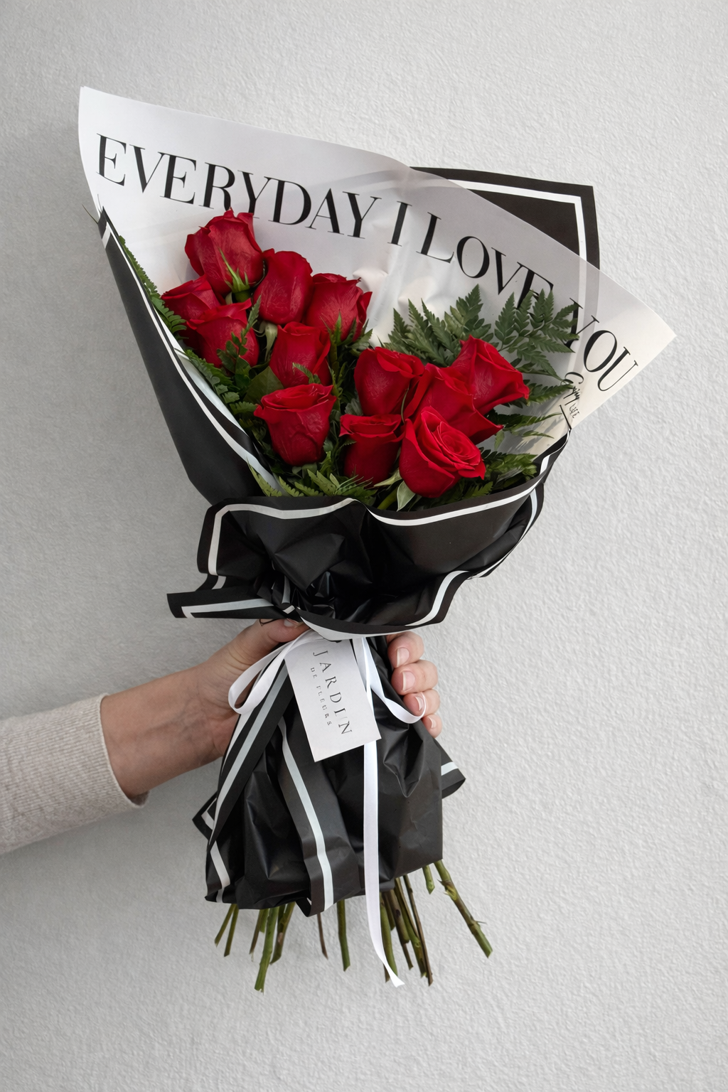 Bouquet of red roses wrapped in black paper with a white ribbon, held against a light gray background.