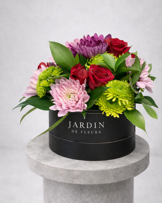 Floral arrangement in a black box labeled 'Jardin de Fleurs' on a gray pedestal.