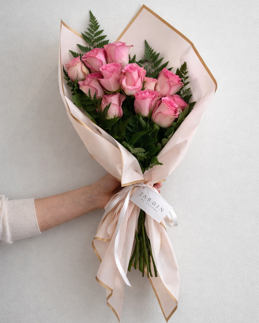 Bouquet of pink roses with a white ribbon held by a person on a light gray background