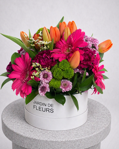 Colorful bouquet of flowers in a white box labeled 'Jardin de Fleurs' on a gray pedestal.