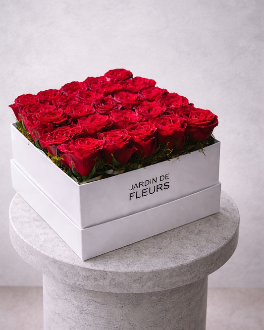 White box of red roses labeled 'Jardin de Fleurs' on a gray pedestal against a light gray background