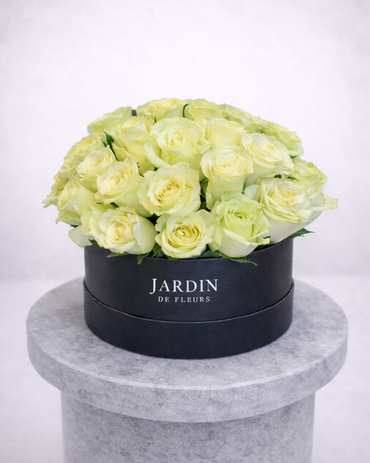 Black box with light green roses labeled 'Jardin de Fleurs' on a gray pedestal against a white background