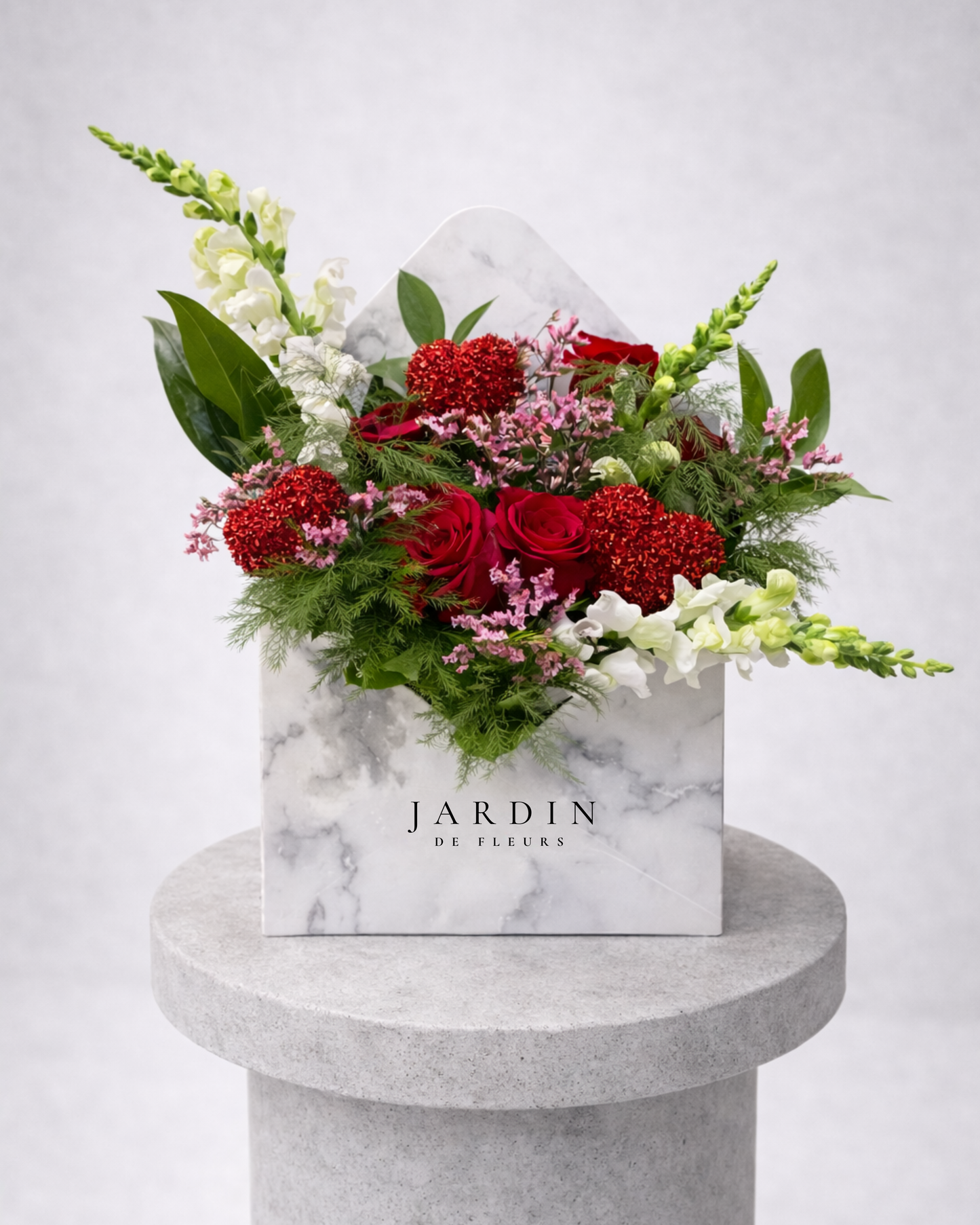 Floral arrangement in a marble-patterned box with 'Jardin' branding on a gray pedestal.
