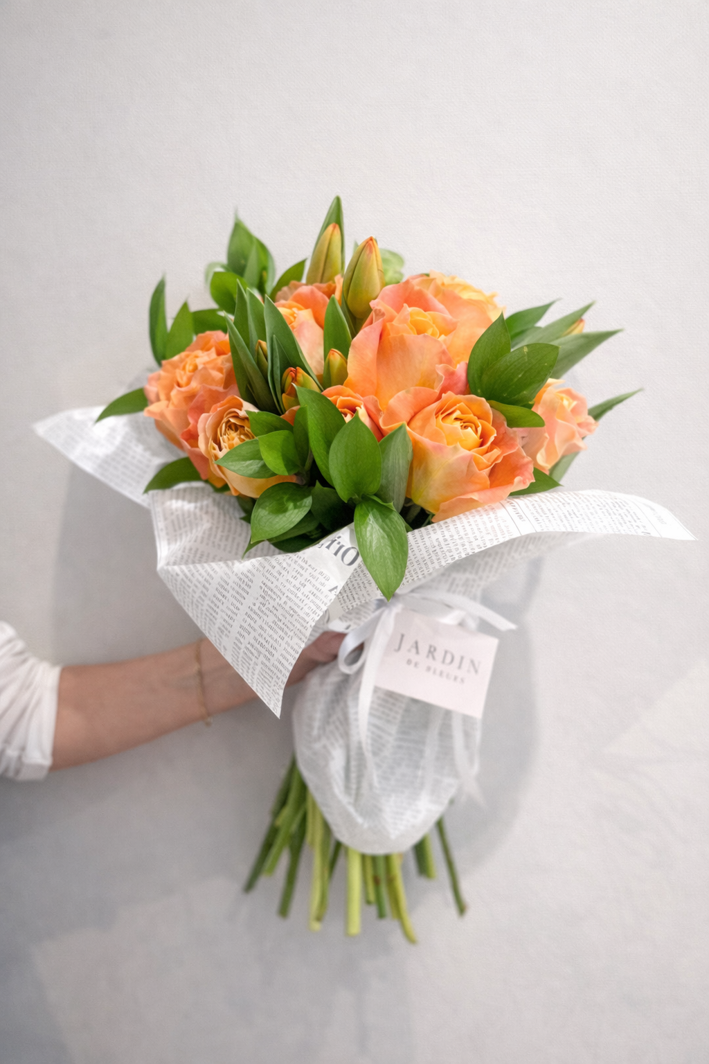 Bouquet of orange flowers wrapped in white paper with a visible brand label on a light gray background