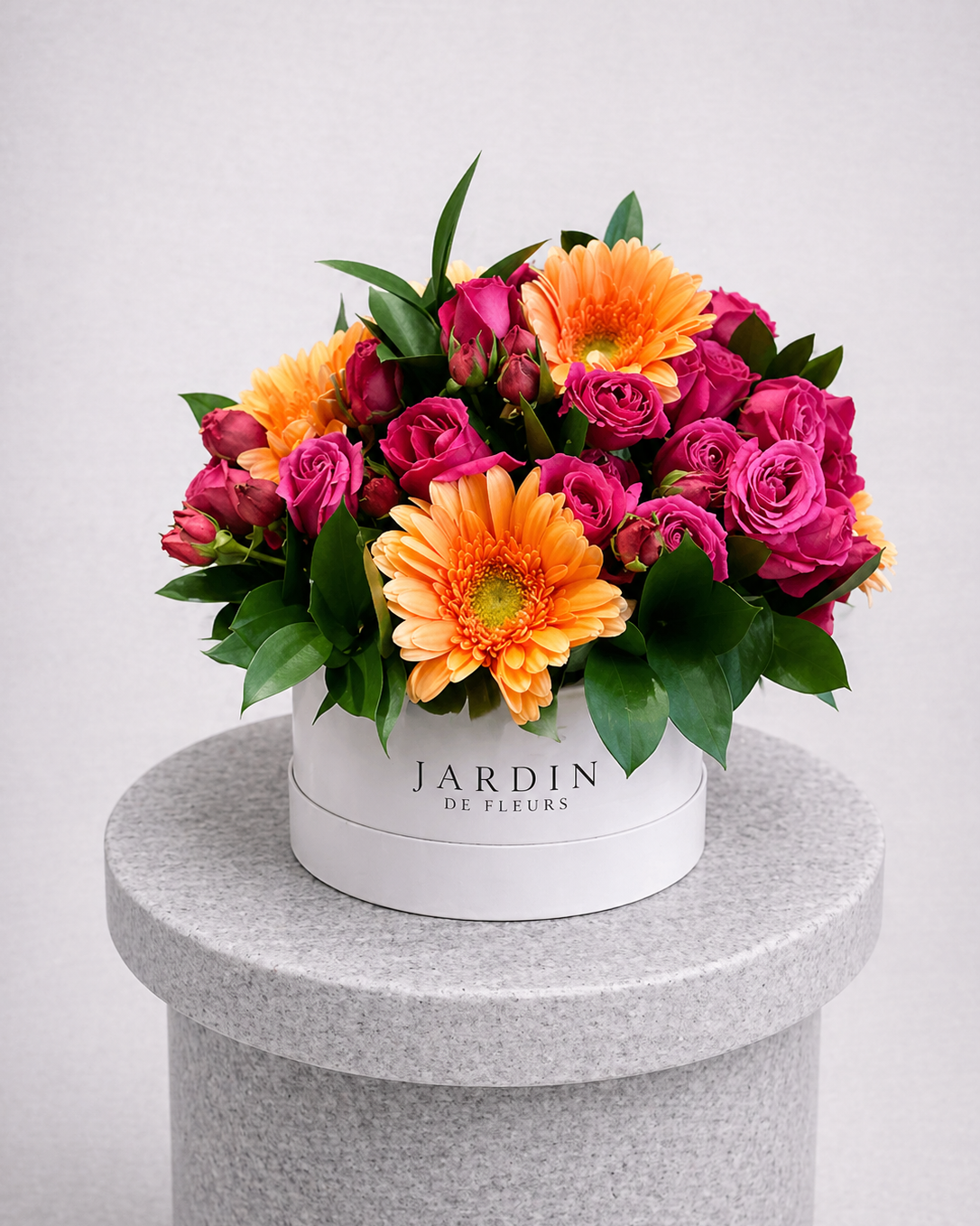 Colorful bouquet of flowers in a white box labeled 'Jardin de Fleur' on a gray pedestal.